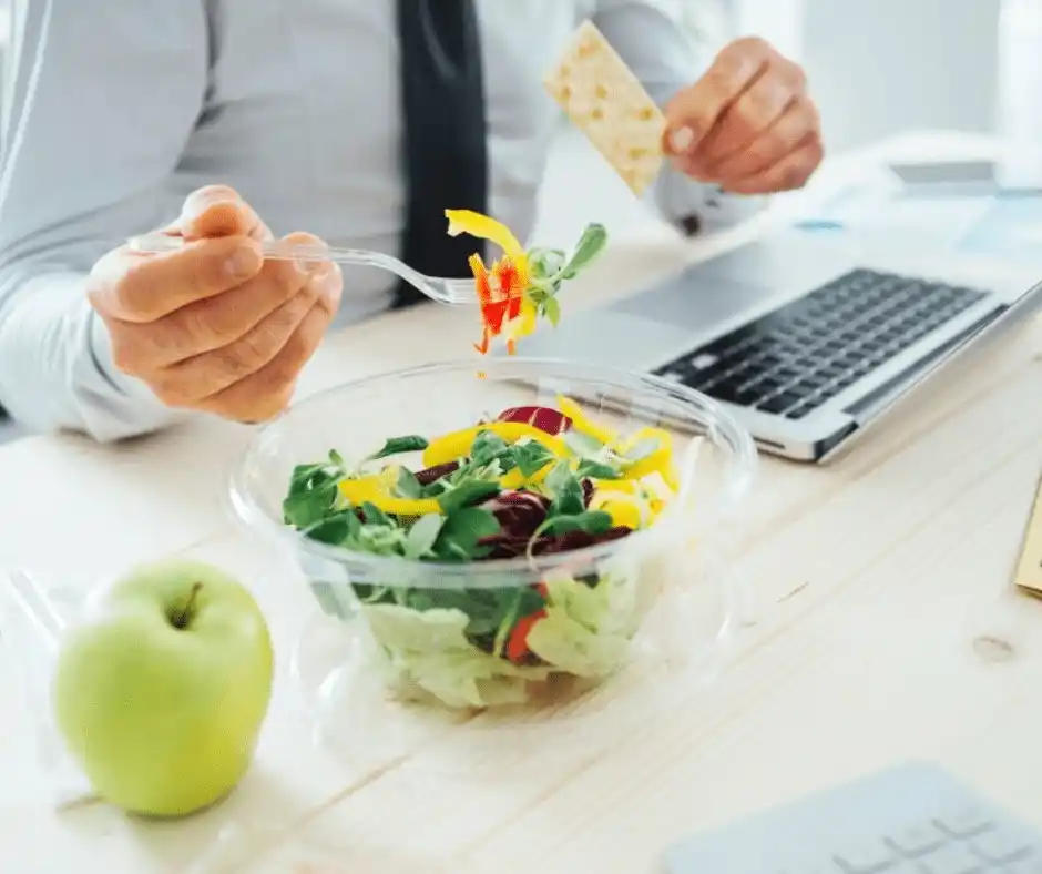 A professional in business attire eats a healthy salad at their desk with a laptop open, symbolizing missed or shortened meal breaks. This represents workplace violations where an employer violates California lunch break laws. Employees should be aware of how long before claiming unpaid breaks in California to protect their rights.
