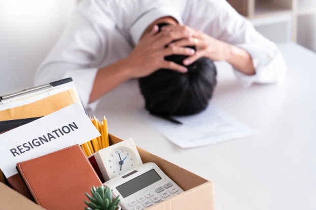 Stressed employee with head in hands next to a box labeled resignation, symbolizing constructive termination.