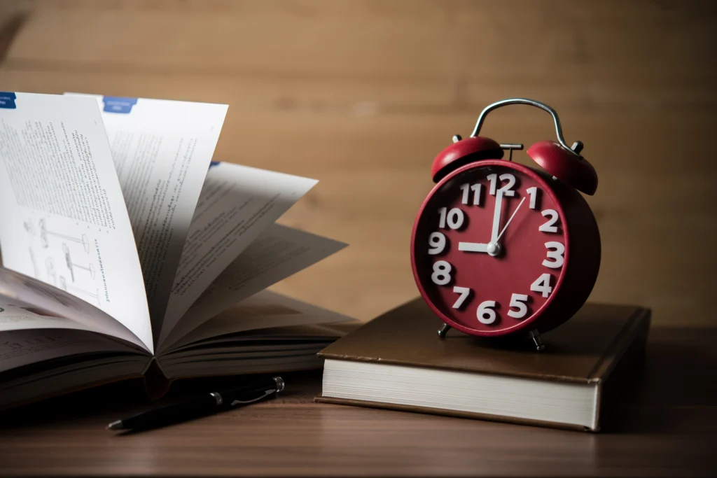 A red alarm clock sits atop a book and pen, highlighting the importance of part-time job hour discussions in California.