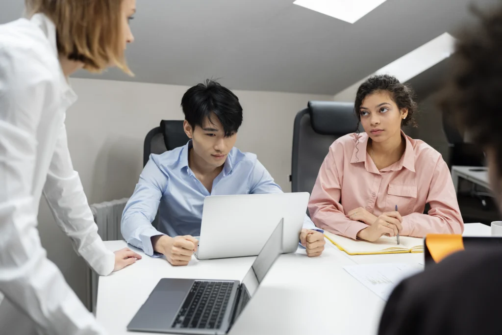 Three individuals seated at a table, each using a laptop, engaged in a discussion about workplace investigations in California.