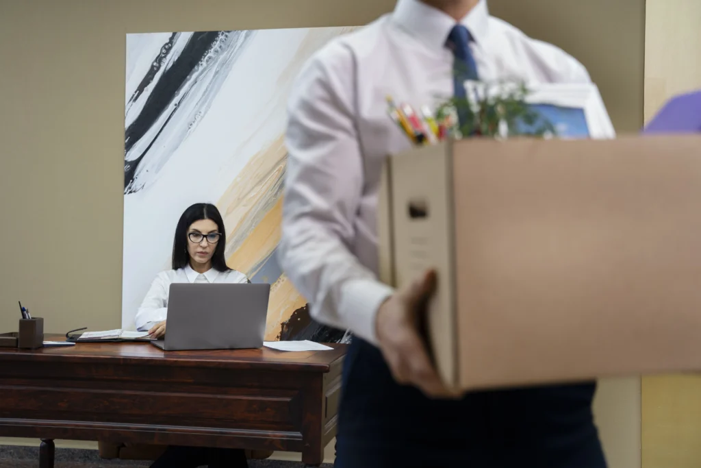 A man in a suit holds a box containing a laptop, symbolizing professional transitions related to termination agreements.