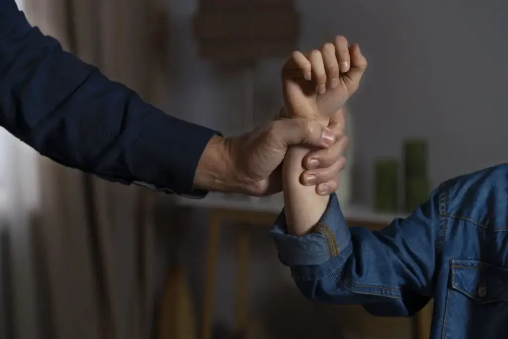 Close-up of an adult holding a child's arm in a dimly lit room, illustrating domestic violence and crime victim protections under California AB 2499 leave laws.