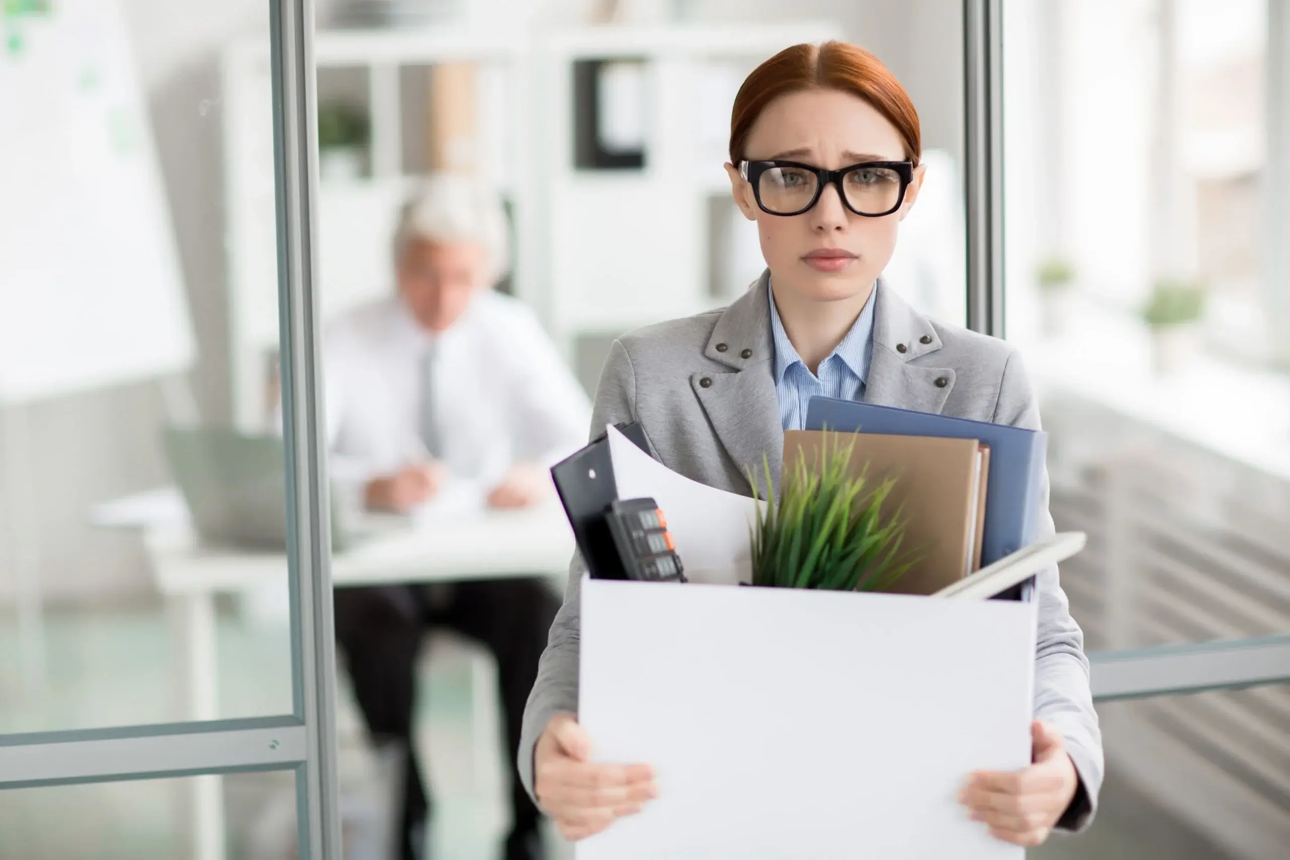 A woman wearing glasses holds a box filled with papers related situation with wrongful termination in California